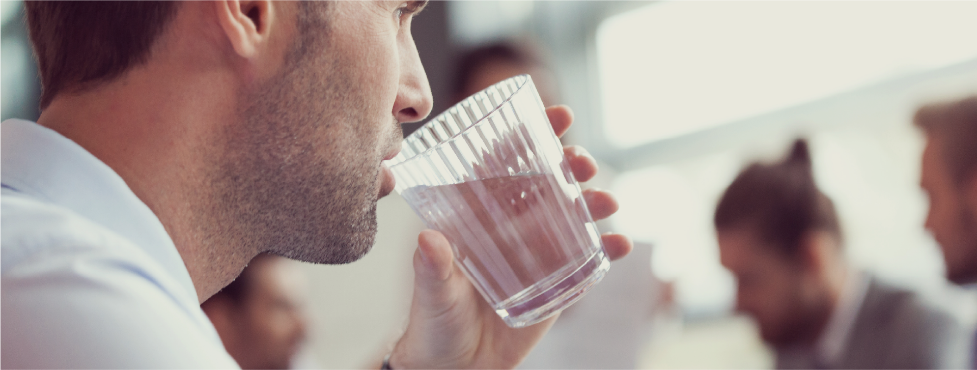 Grianghraf gar-amhairc d’fhear i dtimpeallacht cruinnithe ag ól as gloine trédhearcach uisce.