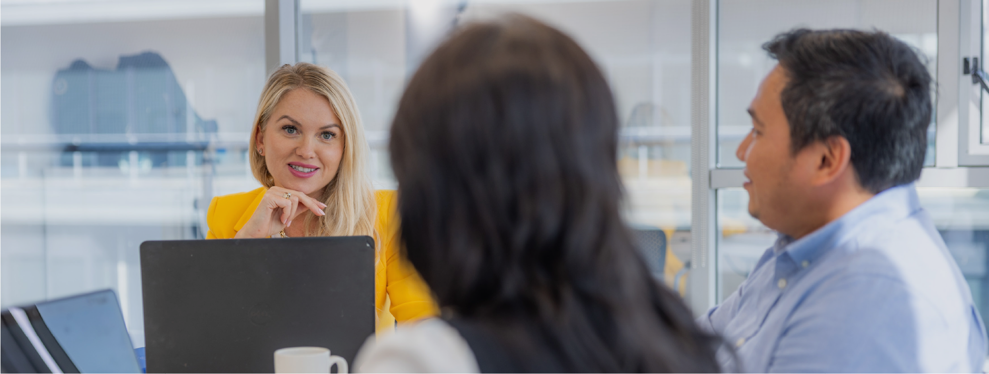 3 dhuine, inscne éagsúil agus eitneacht éagsúil i seomra cruinnithe le ríomhairí glúine.