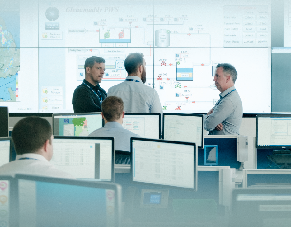 3 fear ina seasamh os comhair scáileáin mhóra iolracha a léiríonn scéimreach oibreacha uisce.