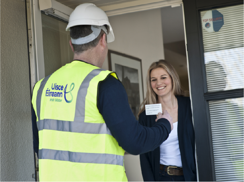 Ionadaí Uisce Éireann ag taispeáint cárta aitheantais agus áititheoir baineann ón teach ag beannú dó.