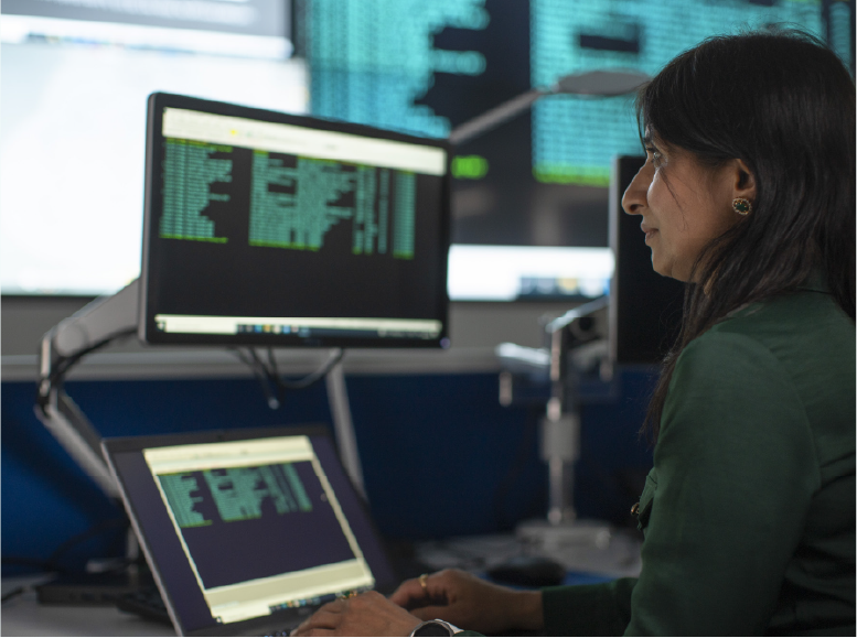 Bean le ríomhaire agus scáileán breise ceangailte ag leibhéal na súl i dtimpeallacht oifige.