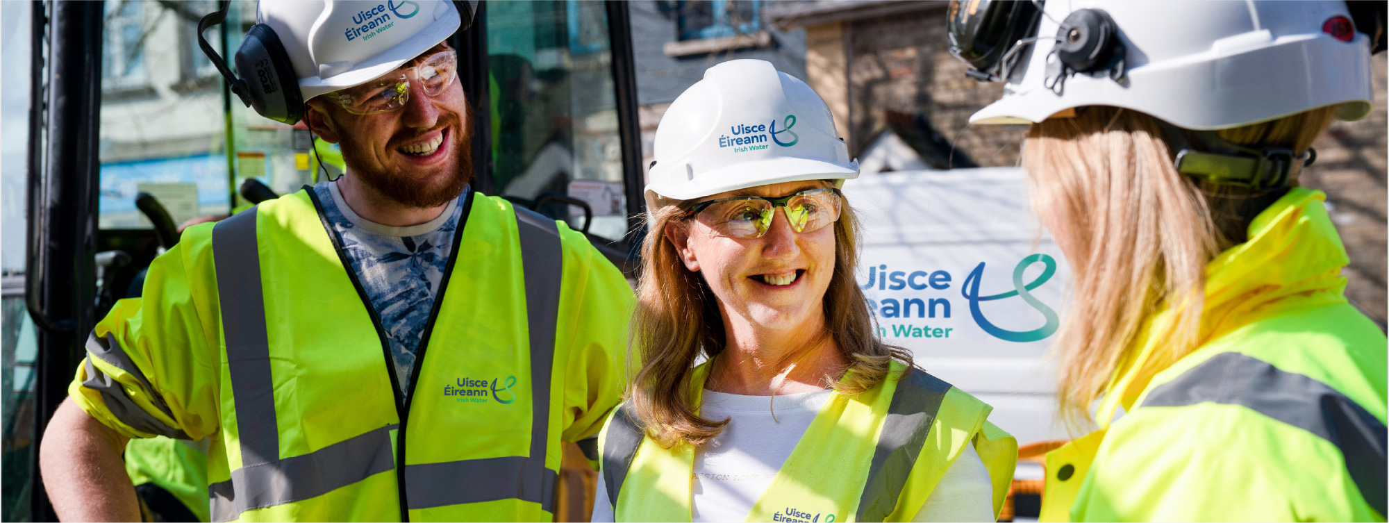 3 innealtóir i mbun comhrá ag suíomh oibreacha lasmuigh agus athbhreithniú á dhéanamh acu ar líníochtaí teicniúla.