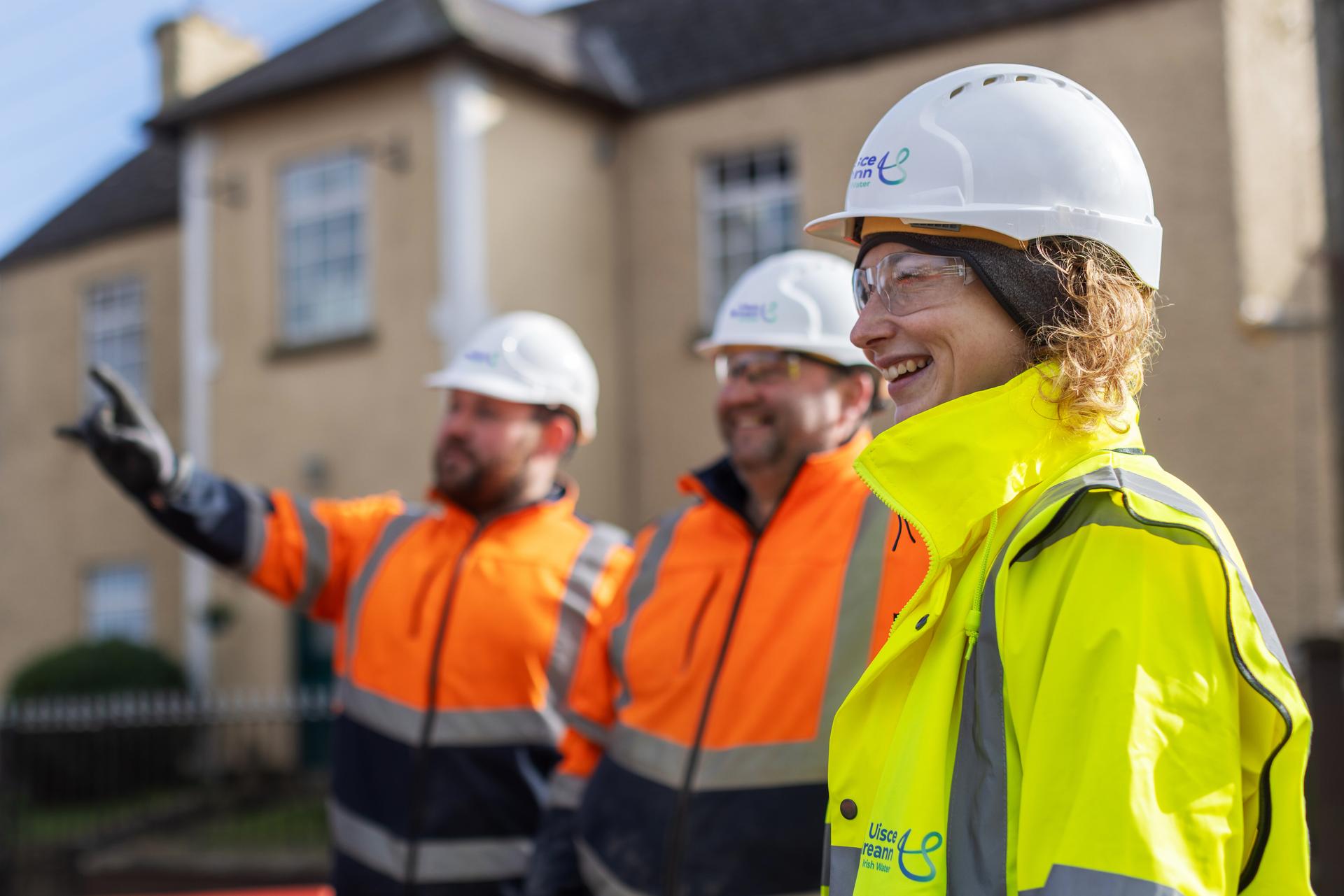 Two engineers wearing orange safety gear and another wearing a yellow high visibility jacket with a helmet