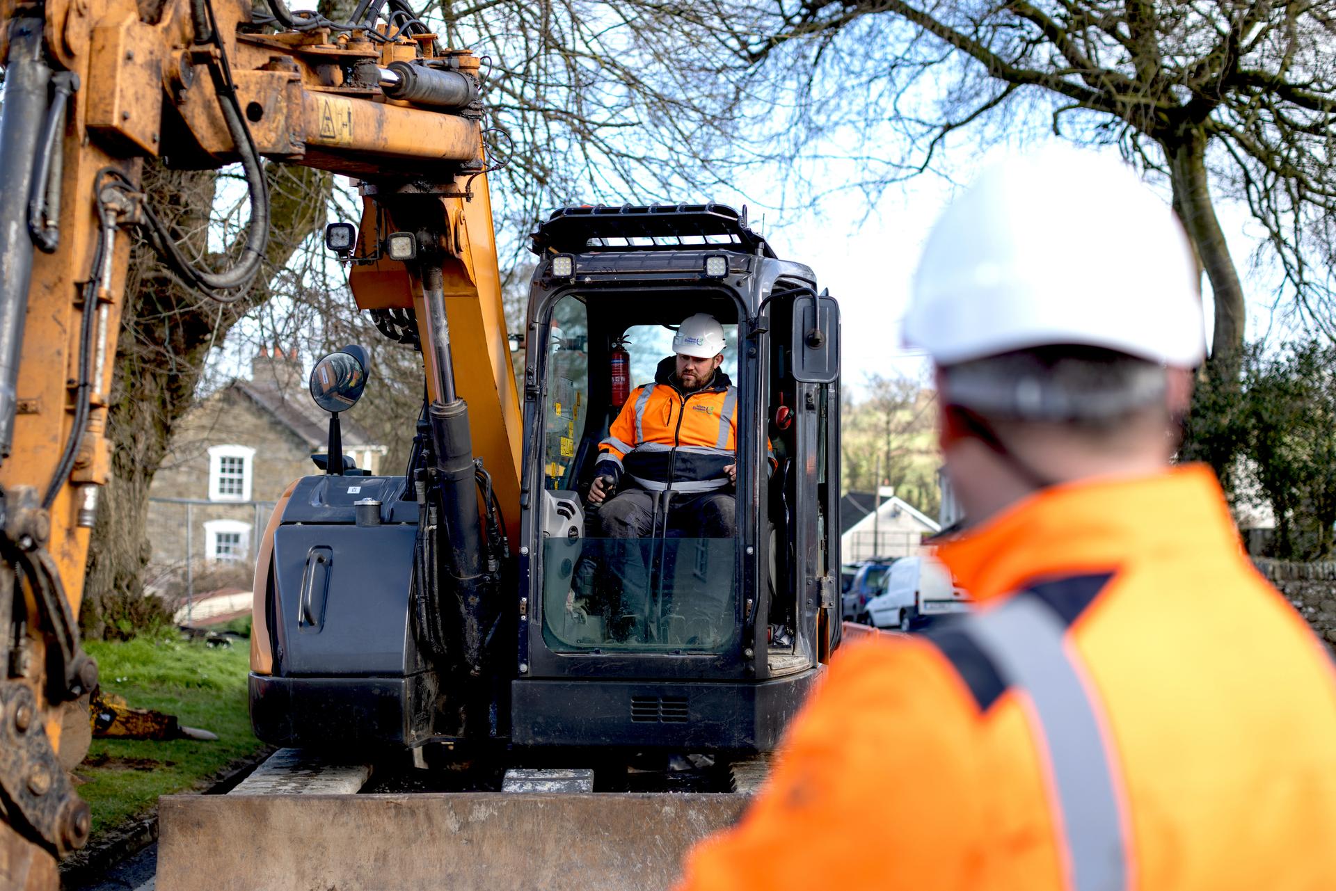 An engineer using a digger and another engineer inspecting the work