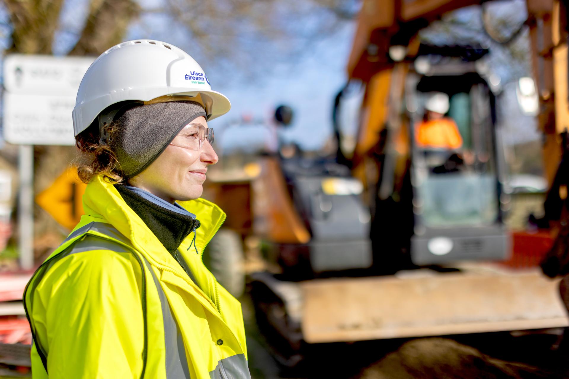 An engineer right beside a digger in works wearing safety gear
