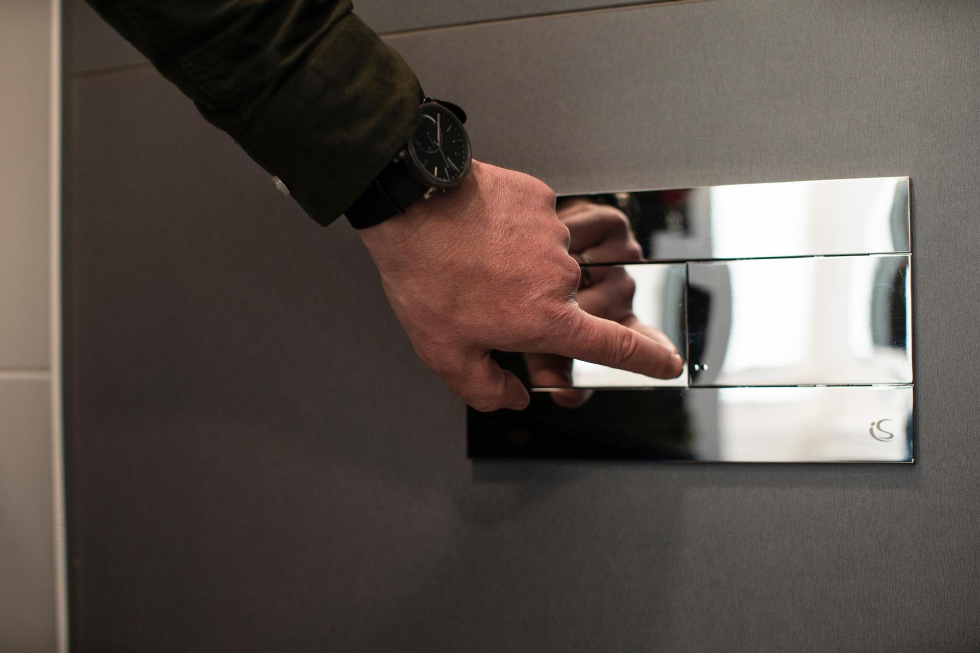 A person pressing a dual flush toilet on the wall