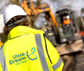 An Uisce Éireann engineer in front of a digger during road works